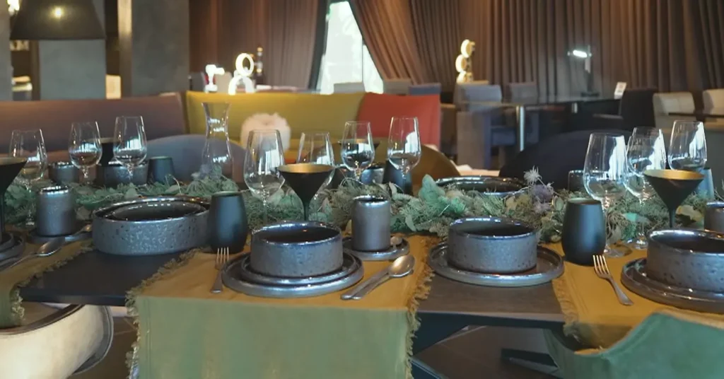Donker aardewerk met kommen, borden en bekers op een gedekte tafel met lopers en groen in de showroom