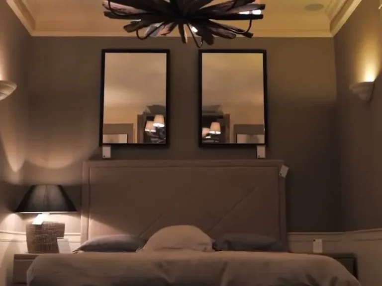 Opgemaakt bed met een gestoffeerd hoofdbord, twee spiegels en nachtlampjes in een slaapkamer in de showroom