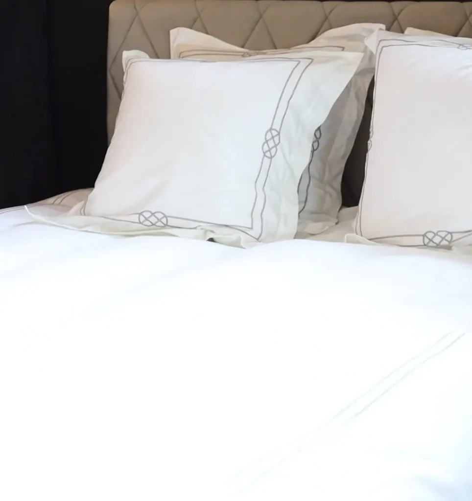 Handen die witte hoofdkussens met geborduurde rand schikken op een bed met wit dekbed