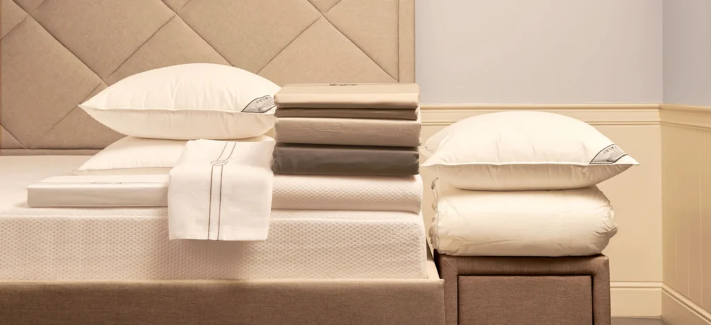Boxspring met ruitvormig gestoffeerd hoofdbord, gestapeld bedlinnen en witte kussens in een lichte slaapkamer