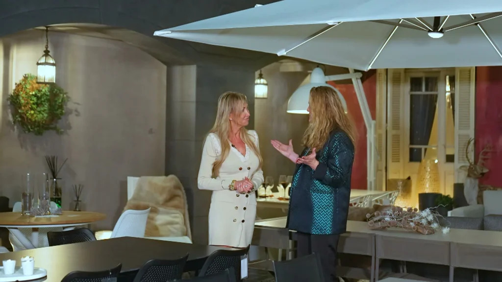 Twee vrouwen in gesprek tussen tuintafels en stoelen onder een zweefparasol in de buitenopstelling van de showroom