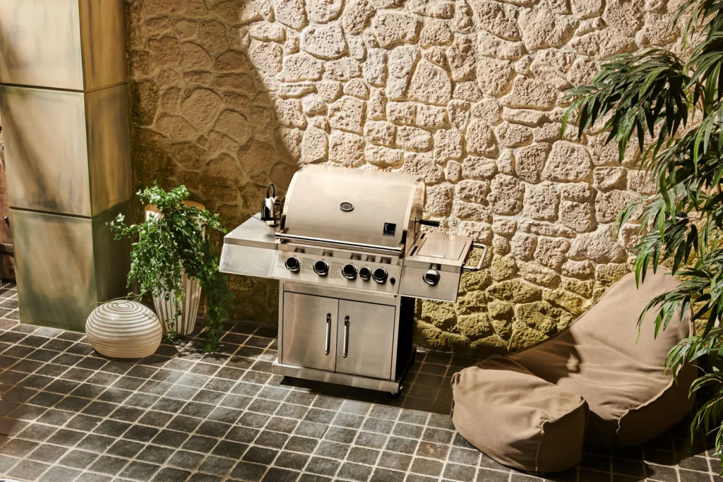 Gasbarbecue in roestvrij staal met een beige zitzak en planten op een terras tegen een natuurstenen muur