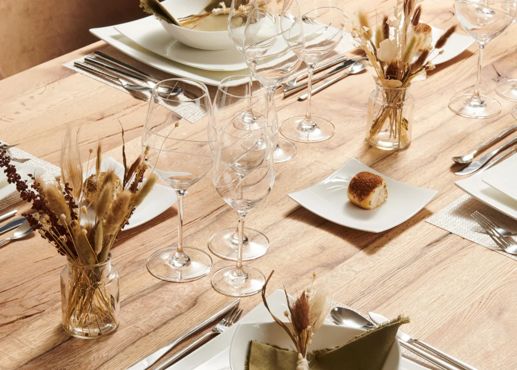 Gedekte eiken tafel met wit porseleinen servies, kristallen glazen, bestek en droogbloemen in glazen vaasjes