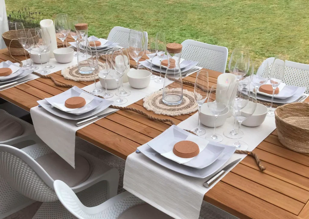 Gedekte houten tuintafel met witte stoelen in het gras, met wit servies, glazen, lopers en kaarsen