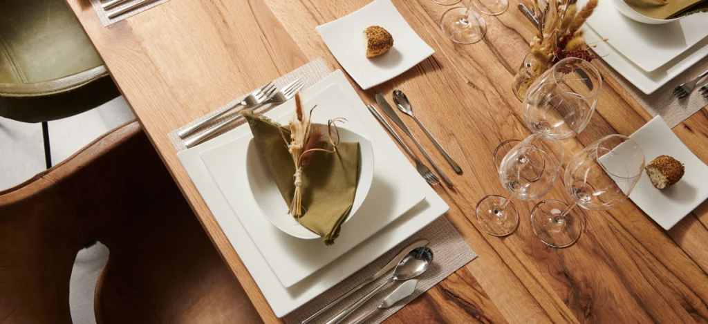Brede kijk op een gedekte houten tafel met wit servies, gevouwen servetten, glazen en droogbloemen