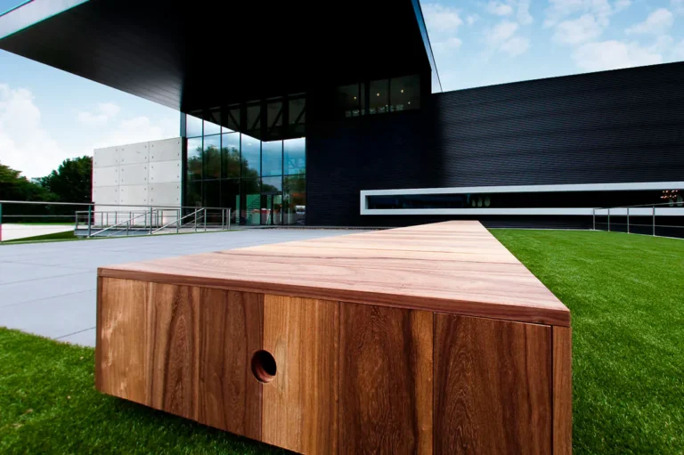 Zwart gebouw van T&T Design in Ternat met grote glazen gevel, gras en een houten zitbank