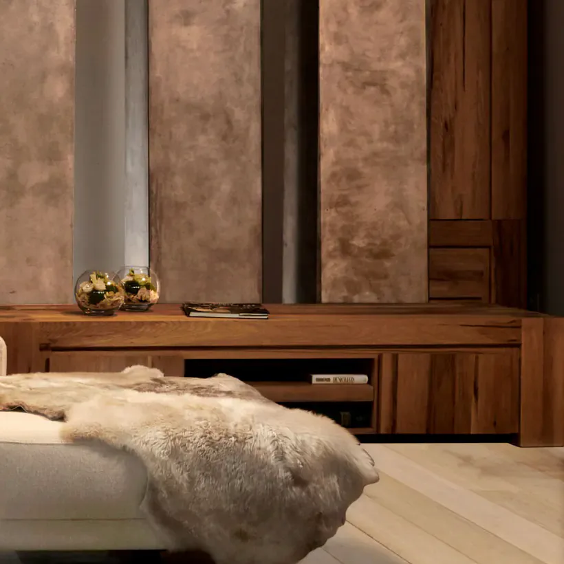 Houten dressoir en hoge houten kast voor bronskleurige wandpanelen in de showroom, met een poef met vacht op de voorgrond