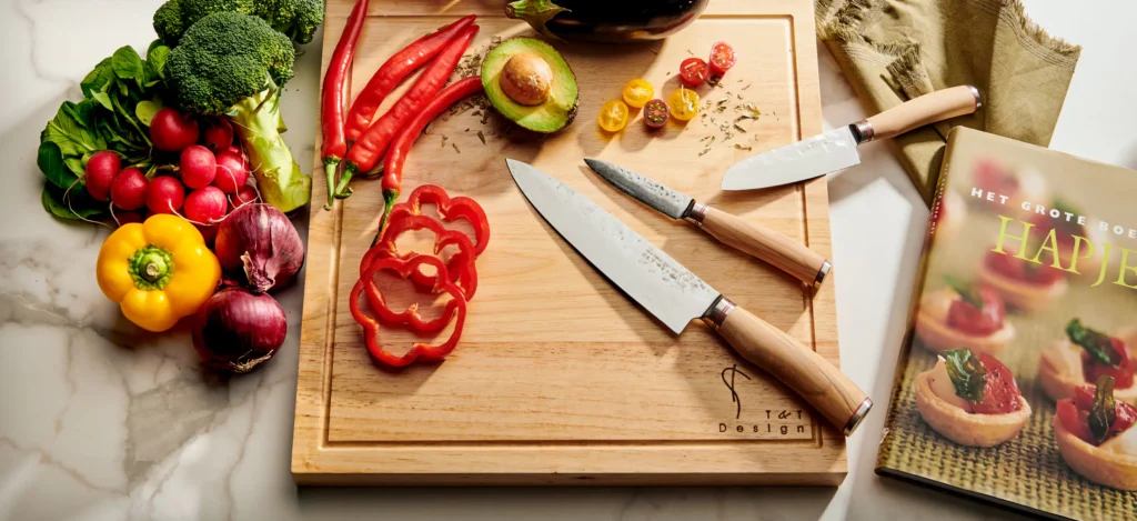Japanse messen met houten heft op een houten snijplank met gesneden paprika, tomaten en kruiden, brede kijk