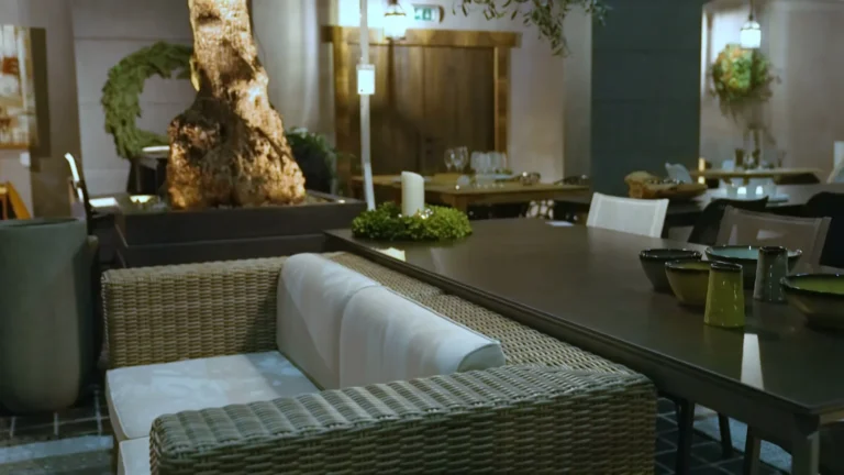 Loungeset in grijs wicker met lichte kussens naast een donkere tuintafel in een buitenopstelling van de showroom