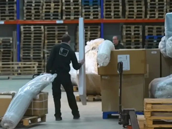 Medewerker van T&T Design zet ingepakte meubels klaar tussen dozen en palletrekken in het magazijn
