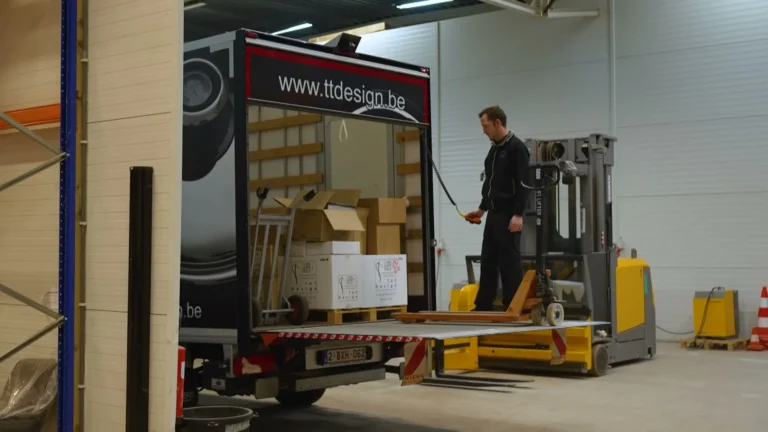 Medewerker laadt dozen met een heftruck in een vrachtwagen van T&T Design in het magazijn