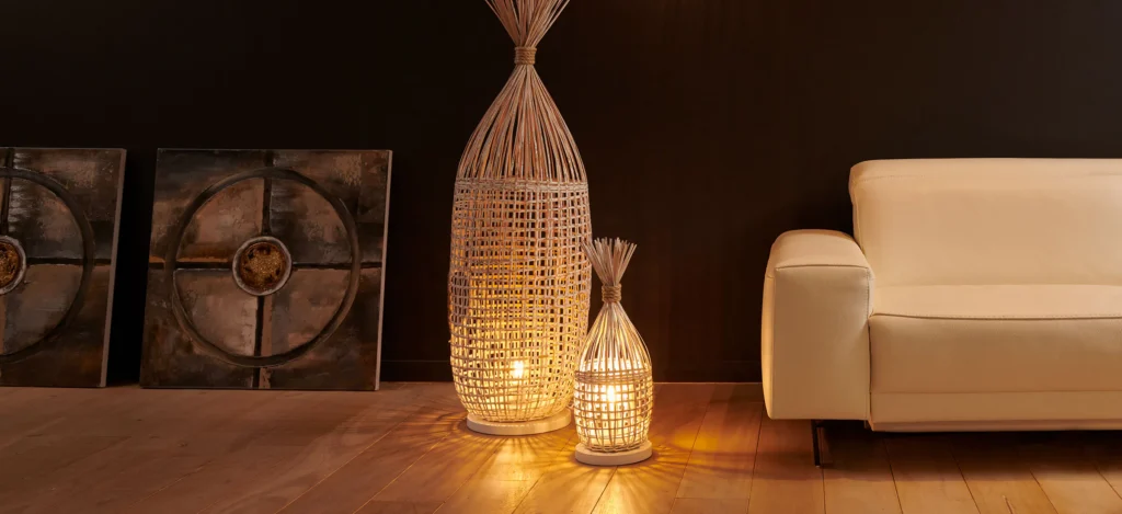 Rieten vloerlampen en hanglamp met warm licht naast een lichte lederen zetel, met wanddecoratie tegen een donkere muur