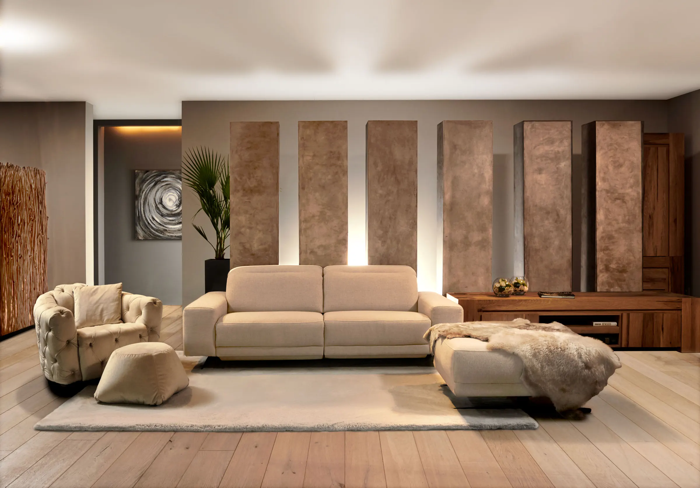 Lichte salon met beige driezit, capitonfauteuil, poef met vacht en bronskleurige wandpanelen in warm licht