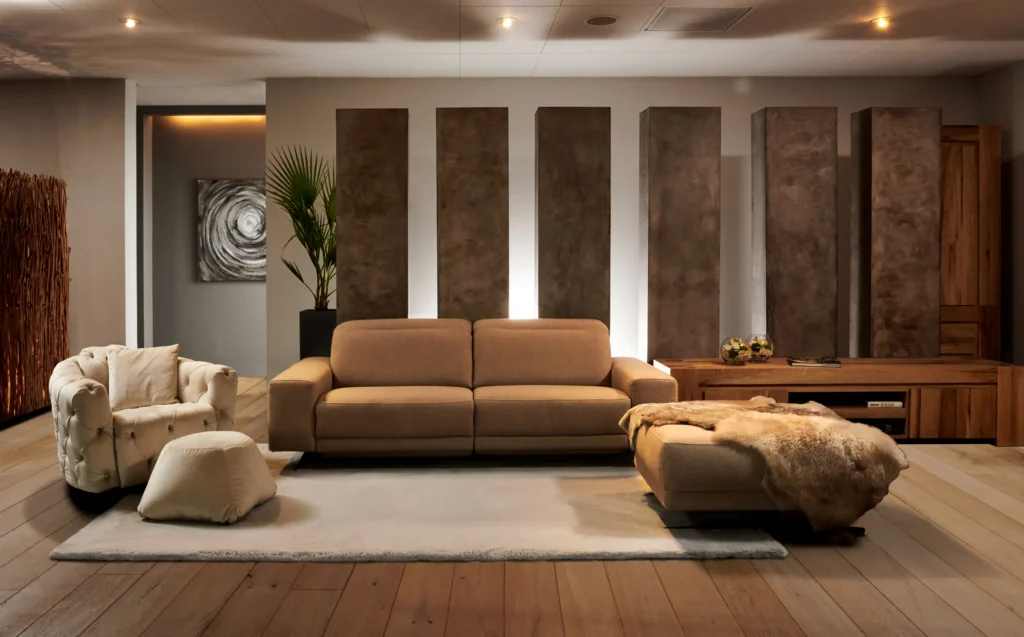 Salon met cognackleurige driezit, capitonfauteuil, poef met vacht en houten dressoir voor bronskleurige wandpanelen