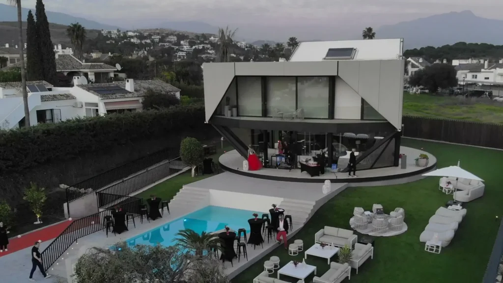 Luchtbeeld van een moderne villa met zwembad, gazon en witte loungemeubelen in een heuvelachtige Spaanse omgeving