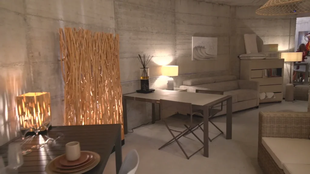 Woonruimte met betonwanden, een tafel, zetel, lampen en een scheidingswand uit natuurlijke houten takken
