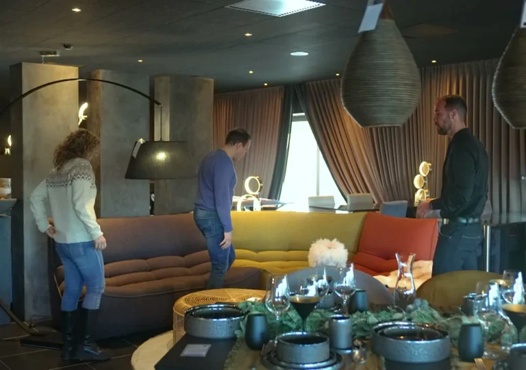Klanten en een adviseur tussen zetels in warme kleuren en gedekte tafels onder rieten hanglampen in de showroom