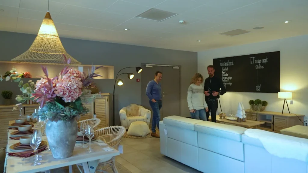 Lichte showroom met een witte lederen zetel en een gedekte tafel, waar een adviseur een koppel rondleidt