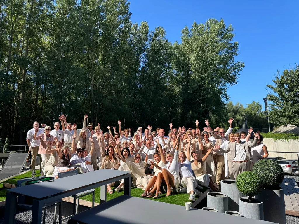 Groot team van T&T Design in lichte kledij, samen buiten in de zon bij een terras met tuinmeubelen