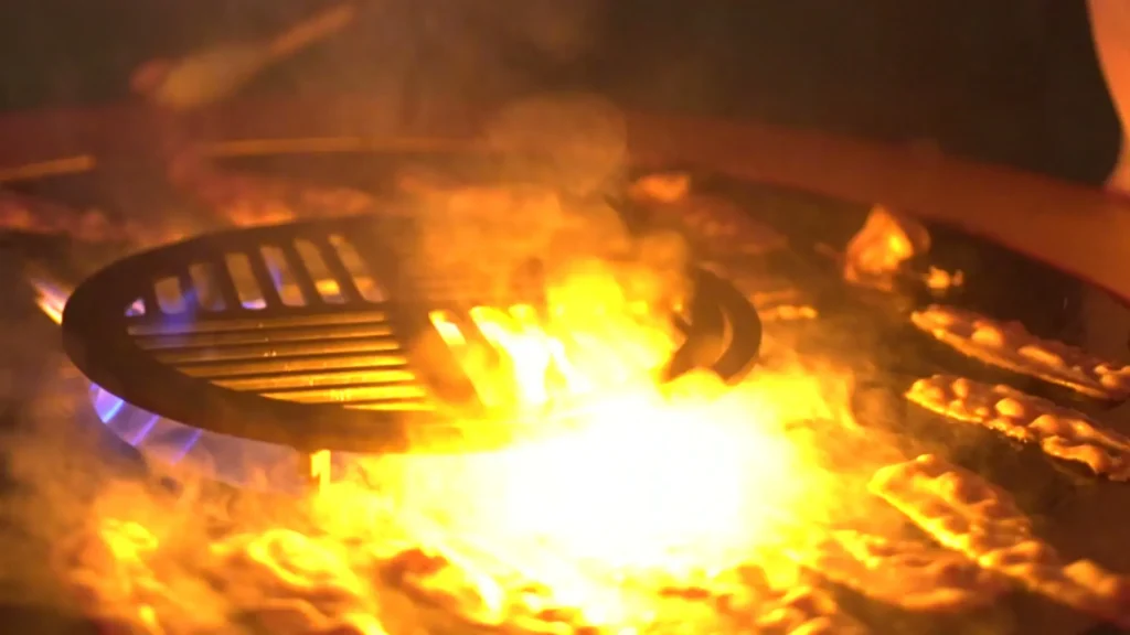 Hoge vlammen en gloed op de bakplaat van een vuurschaal met grillrooster, in het donker