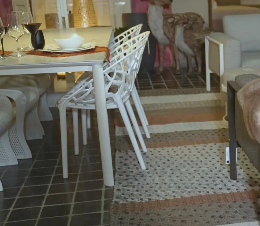 Witte tuinstoelen met opengewerkte rug aan een gedekte buitentafel in de buitenopstelling van de showroom