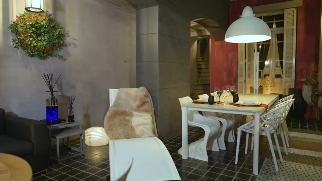 Witte tuintafel met witte stoelen en een ligstoel met vacht onder een witte hanglamp in een buitenopstelling