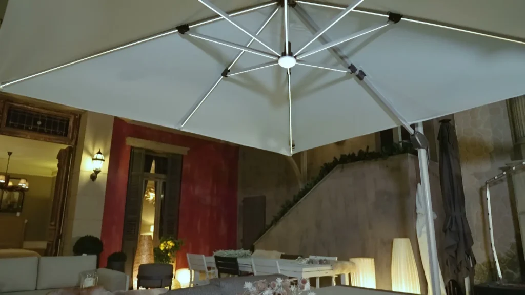 Grote witte zweefparasol boven een gedekte buitentafel, tegen een mediterrane gevel met warm licht