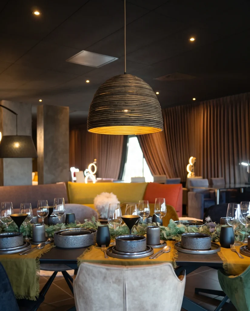 Rieten koepelhanglamp met warm licht boven een gedekte tafel met donker servies, glazen en mosterdgele lopers in de showroom